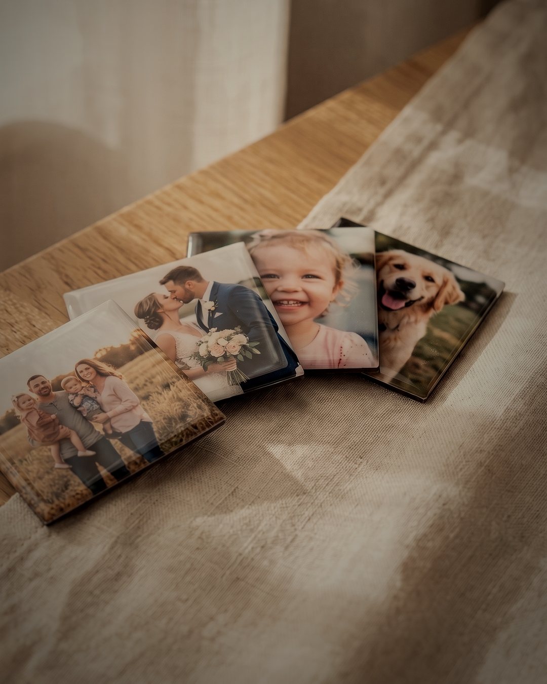 Vier glänzende Fotomagnete mit Familien-, Hochzeits-, Kinder- und Hundefoto auf einem Leinentuch im warmen Licht