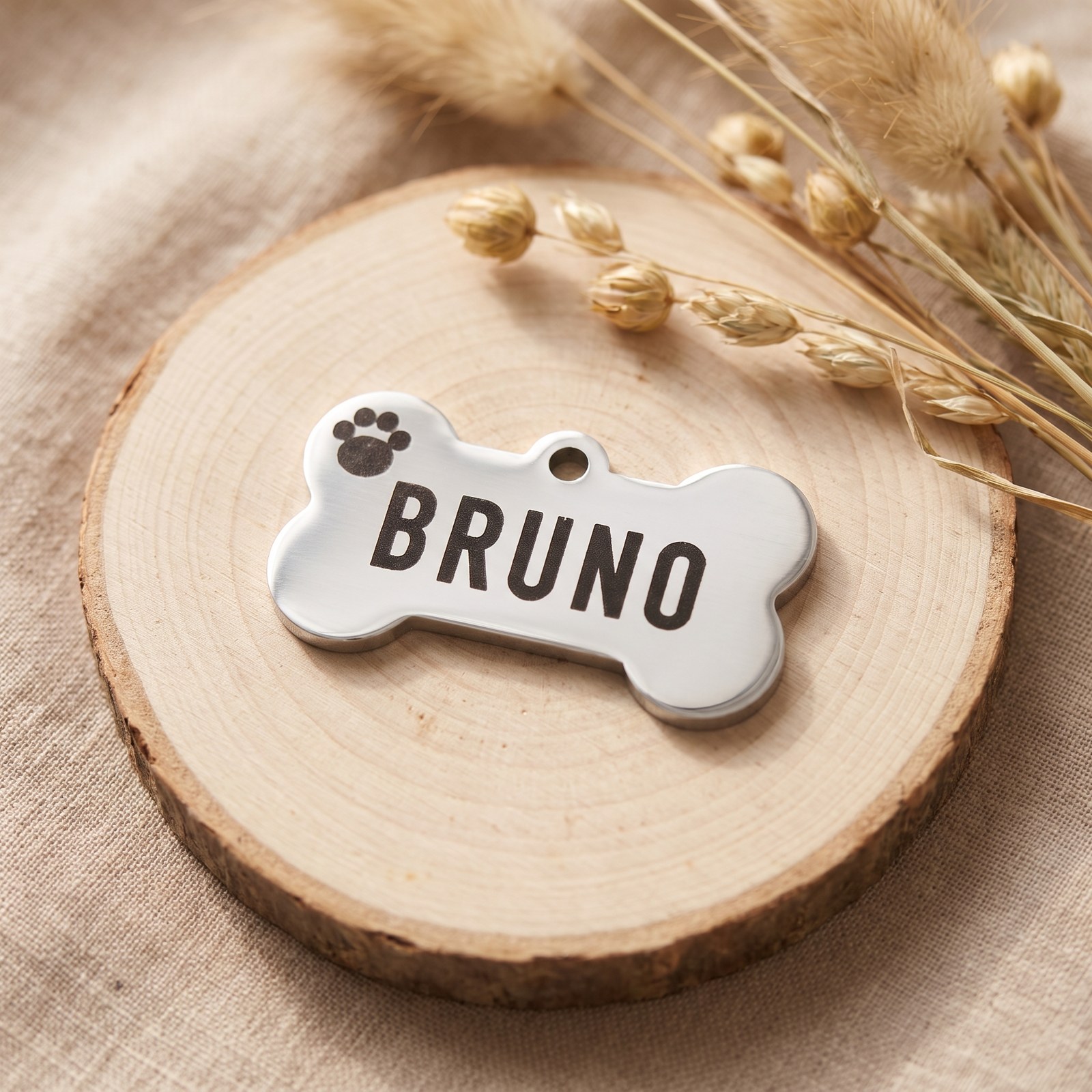Hundemarke in Knochenform aus poliertem Edelstahl mit der Gravur „BRUNO“ und Pfote auf einer Holzscheibe